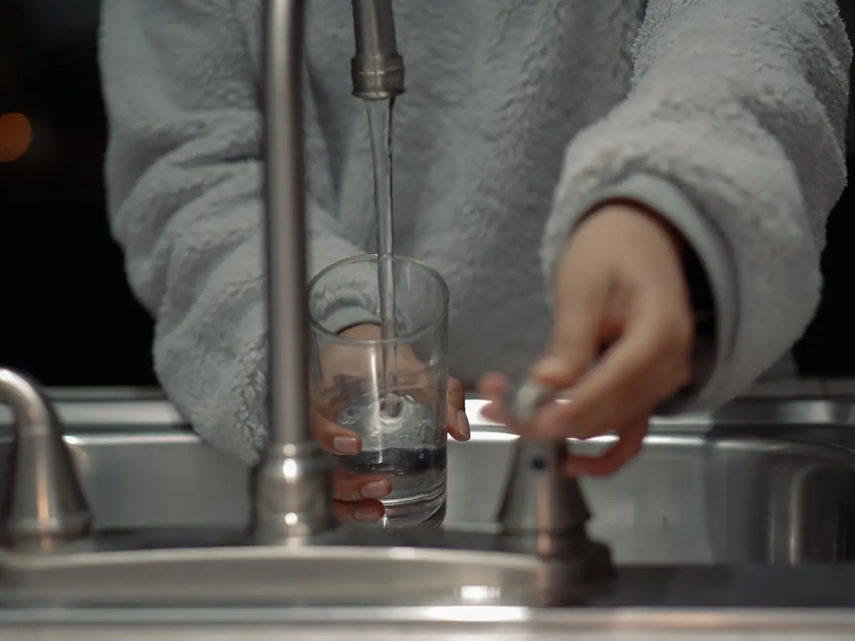 A hand filling a clear drinking glass from a kitchen tap
