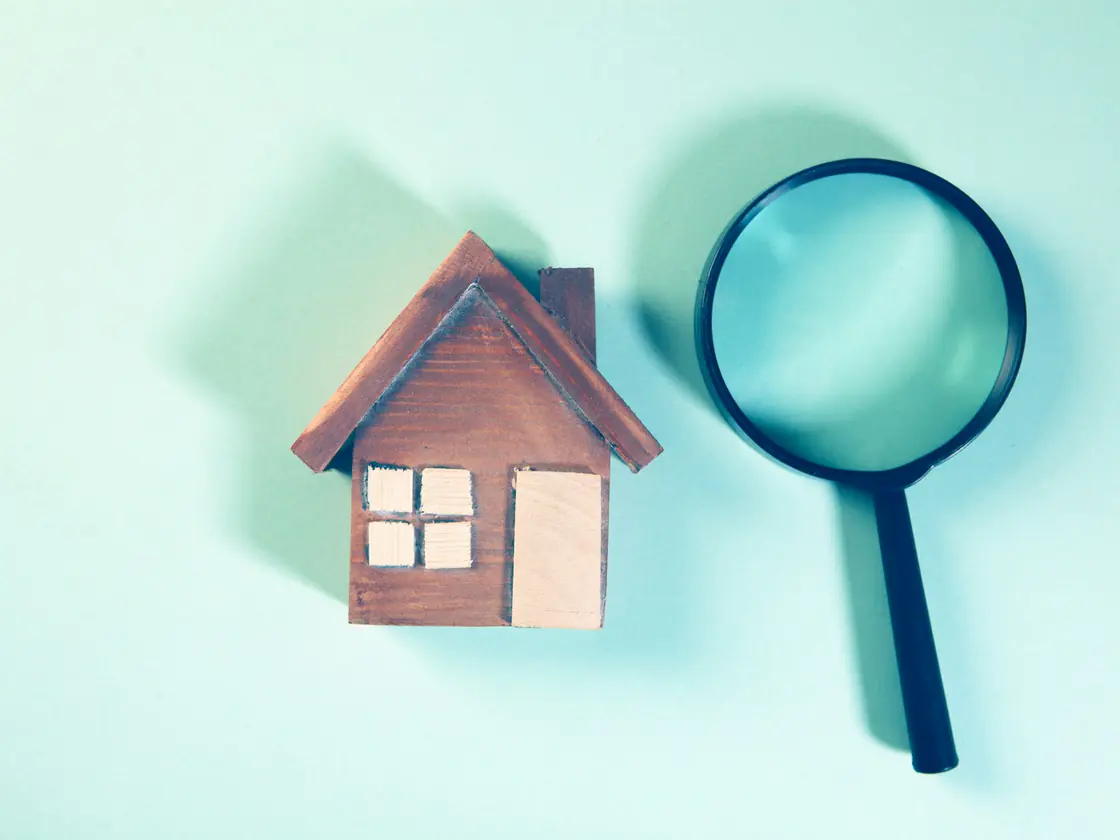 A small wooden model house beside a magnifying glass