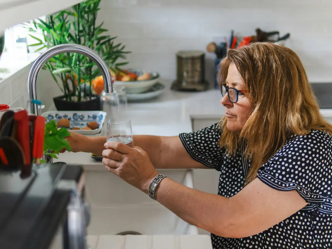 A woman filling a glass with water from her kitchen faucet
