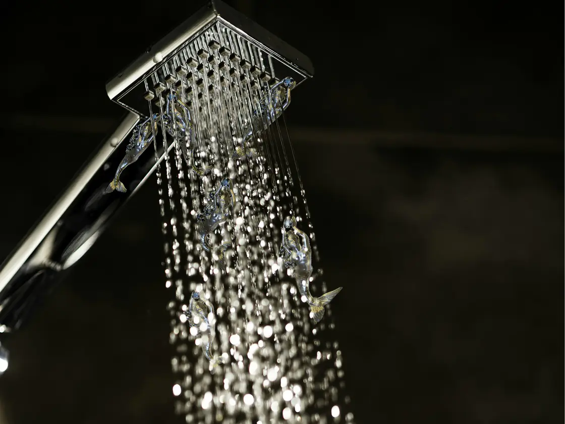 Water pouring from a square shower head against a dark background