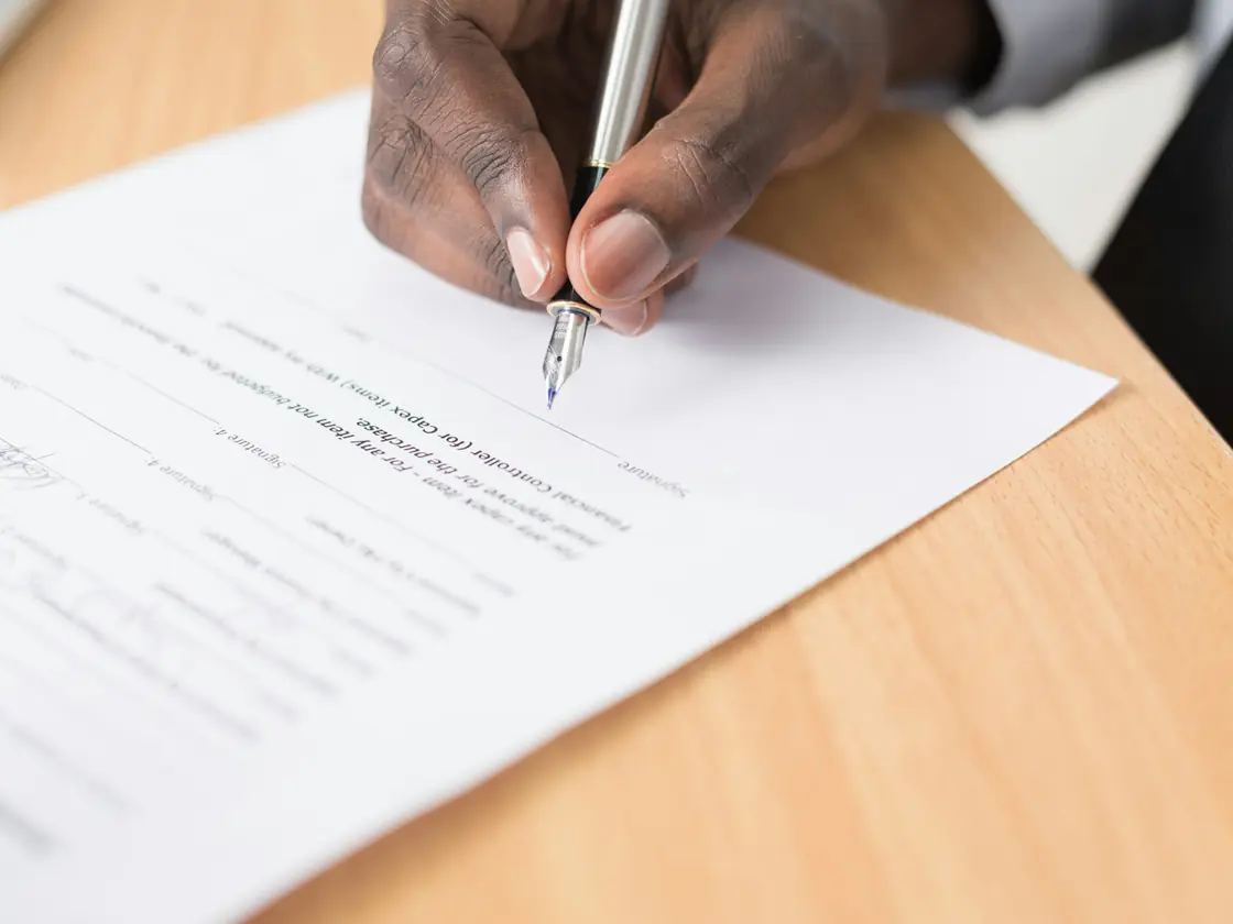 A hand signing a printed document on a wooden desk