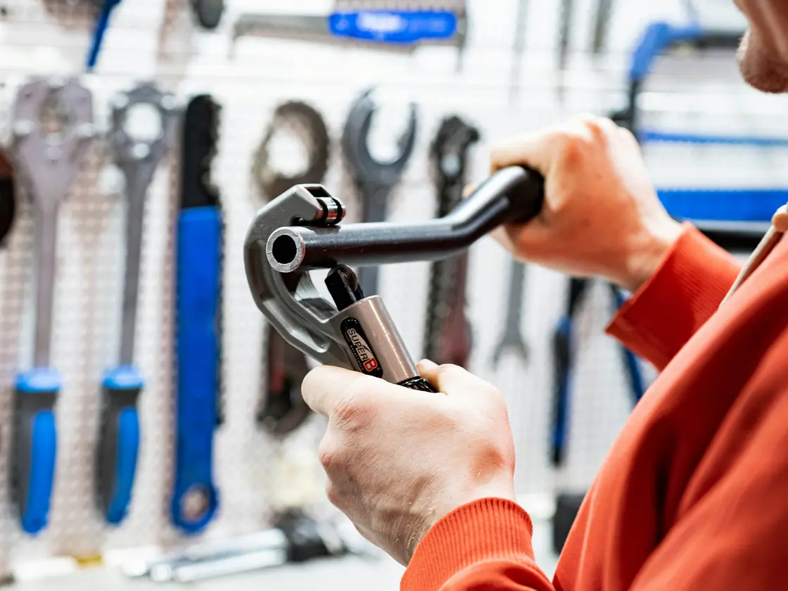A tradesman holding a pipe wrench in front of a wall of tools