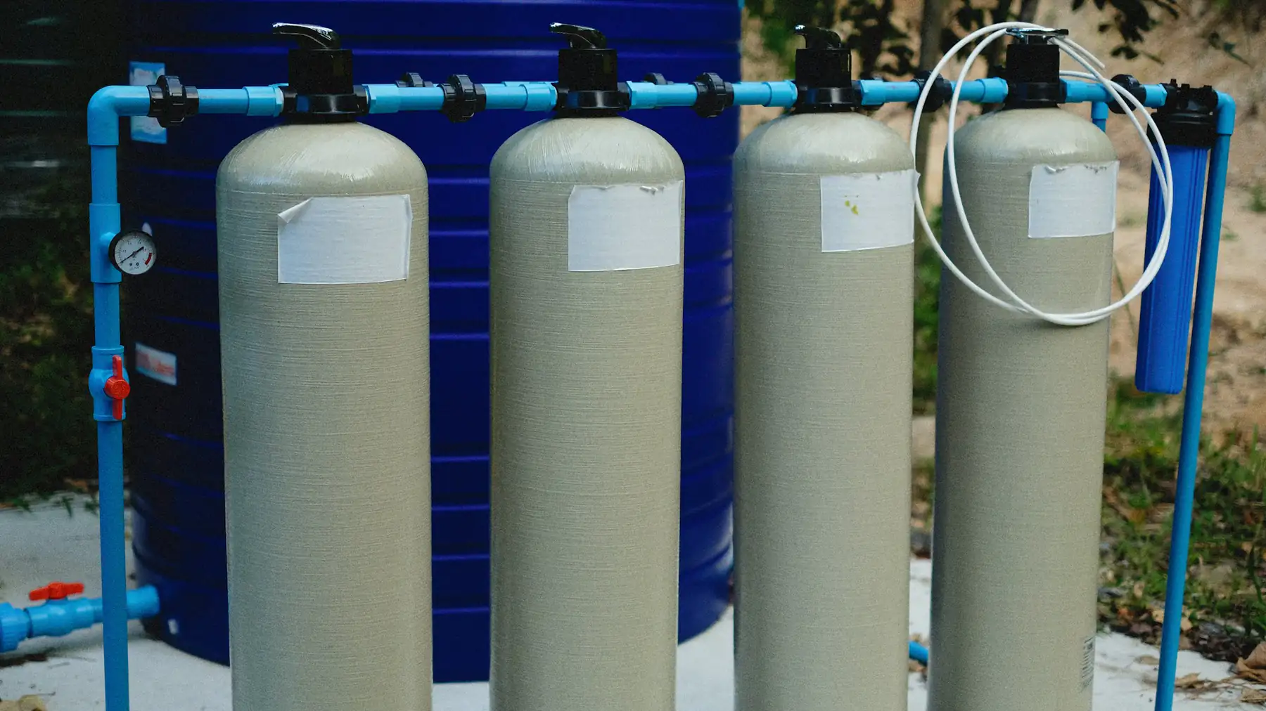 A row of fiberglass water treatment tanks connected by blue pipework
