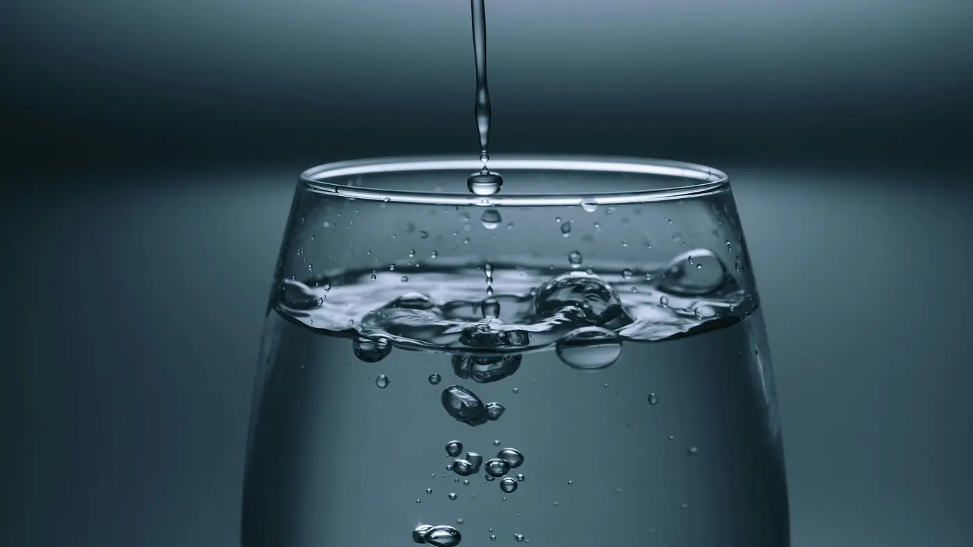 A thin stream of water filling a clear glass against a dark background